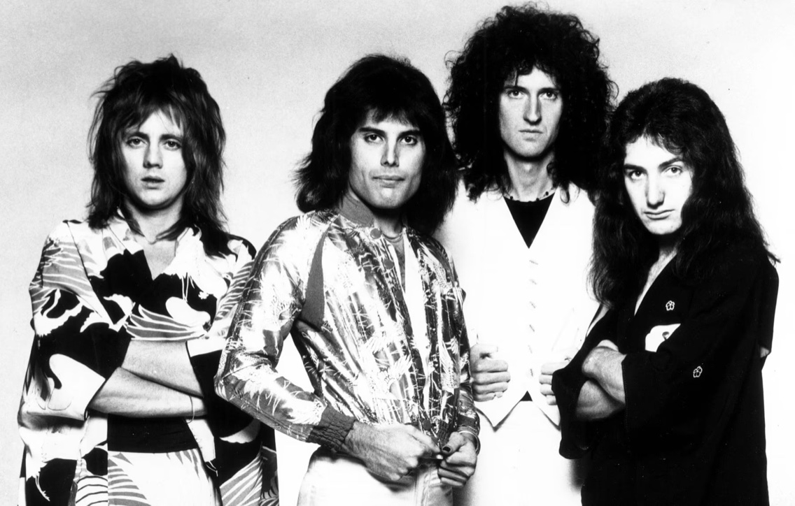 The four members of Queen — Roger Taylor, Freddie Mercury, Brian May, and John Deacon — posing together in a black-and-white 1975 publicity photograph