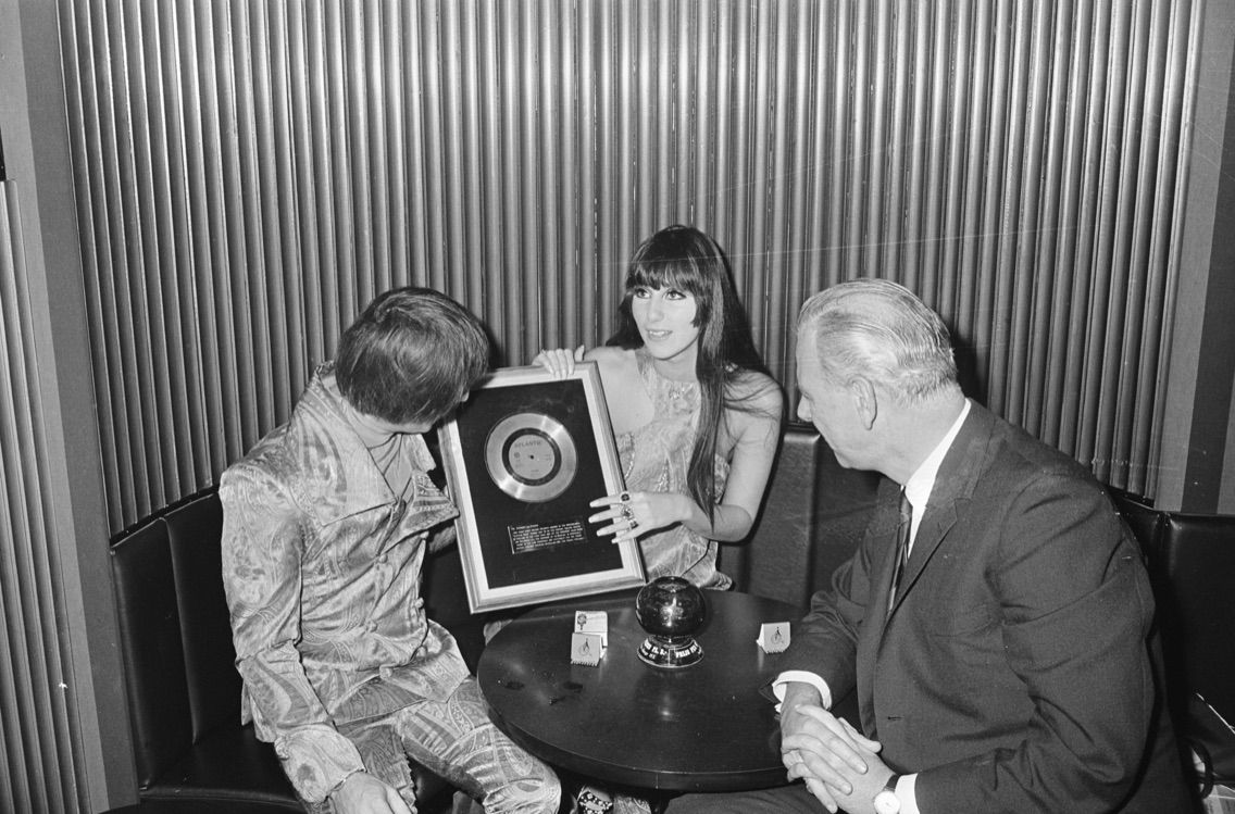 Cher holds a framed gold record while Sonny, in a paisley suit, looks on, 1967